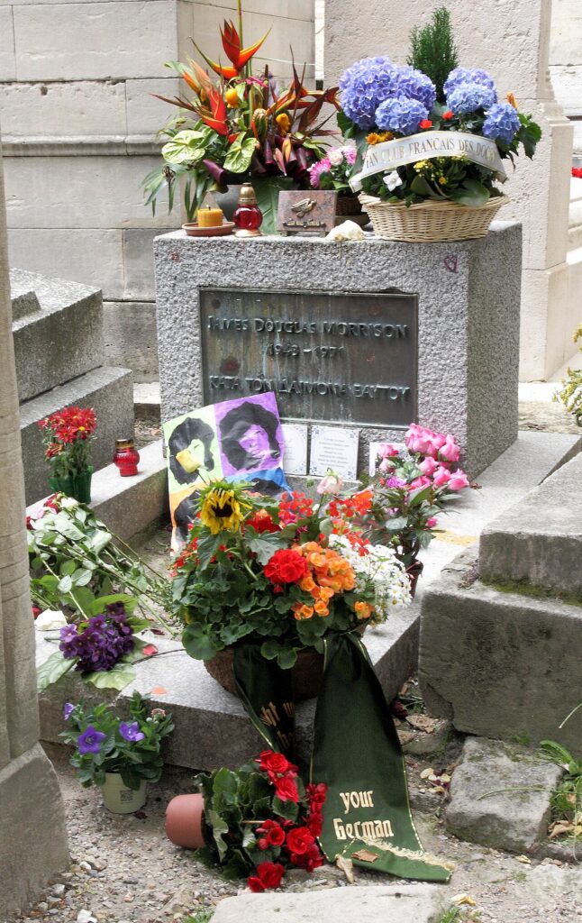 Jim Morrison's gravesite in Père Lachaise Cemetery in Paris, France. The concrete marker is covered in flowers, photos, and detritus.